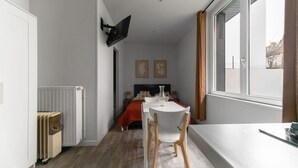 A compact bedroom with a bed, bedside table, and a large window. - Appartement design Centre Ville proche Thermes (Vichy)