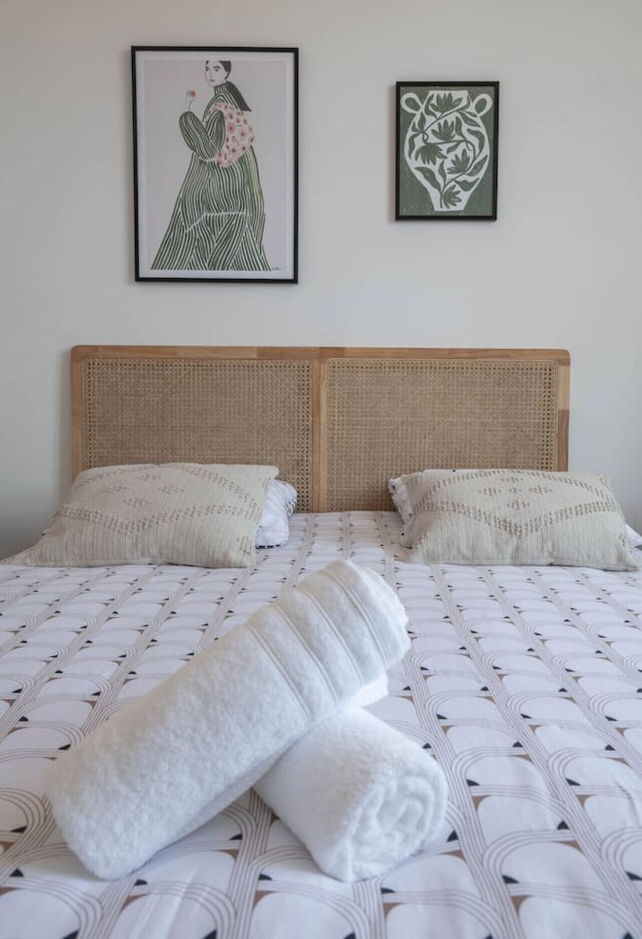 Un letto matrimoniale con testiera intrecciata, due cuscini e una coperta piegata con cura.