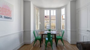 Un comedor con mesa de madera y cuatro sillas verdes, paredes blancas y vistas a través de un ventanal.