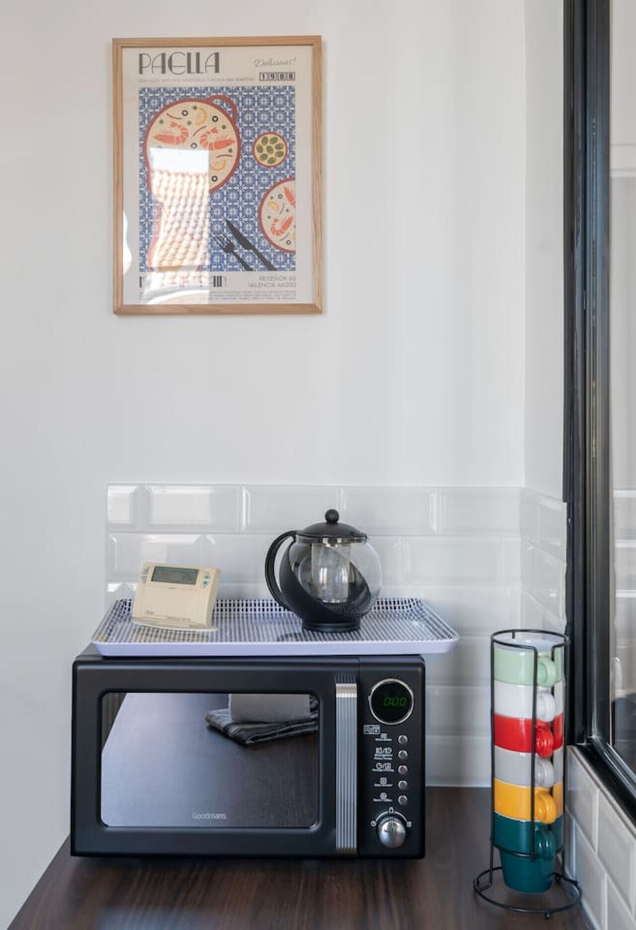Een magnetron met een digitaal display, een waterkoker en een kleurrijke, gestreepte container op een tafel in een keuken.