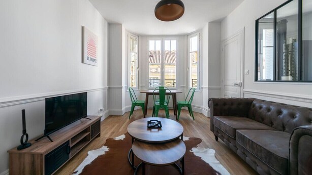 Una sala de estar con televisor, una mesa redonda, un sofá y un ventanal con vistas a edificios.