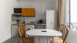 A compact kitchen with a microwave, sink, and cabinets, a dining table with chairs, and a washing machine.