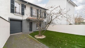 A modern two-story house with a garage, a small tree in the front yard, and a white wall.