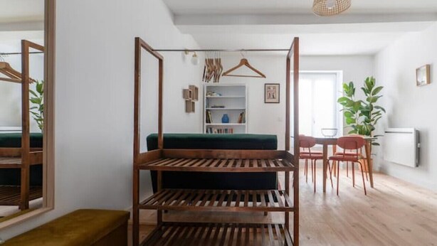 Een moderne, open woonruimte met een houten vloer, een centraal geplaatst bed met een groene hoofdbord, een eethoek met rode stoelen en een grote spiegel aan de linkerkant.