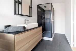 Ein modernes Badezimmer mit einem Holz-Waschtisch, einem weißen Waschbecken und einer Duschkabine.