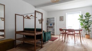 Een kamer met een stapelbed, een eettafel met stoelen, een boekenkast en een groot raam.