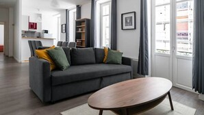 Una sala de estar moderna con un sofá gris, una mesa de centro de madera y una cocina al fondo.