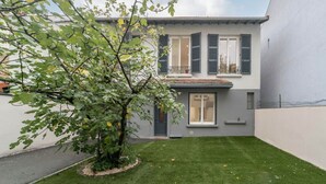 Een modern huis met twee verdiepingen, een kleine voortuin en een boom.
