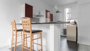 A modern kitchen with a central island, wooden chairs, and white cabinetry.