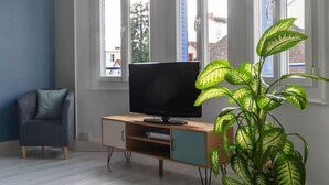 A living room with a TV on a wooden cabinet, a blue armchair, and a large potted plant.