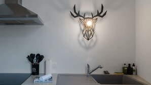 Una cocina con un lavamanos de acero inoxidable, un grifo moderno y una lámpara de pared con forma de cabeza de ciervo.