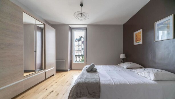 Un dormitorio con cama, un espejo grande, una ventana y una puerta que da a un balcón exterior.
