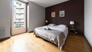 Un dormitorio con cama, dos lámparas de noche, una ventana con vista a un balcón y una lámpara de techo.