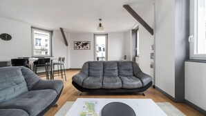 Una sala de estar moderna con un sofá gris, un comedor con mesa y sillas, y una cocina al fondo.