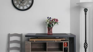 Une pièce comprenant un meuble en bois, une chaise, une horloge murale, un vase avec des fleurs et un lampadaire.
