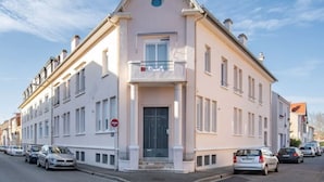 Un bâtiment à deux étages doté d’une façade symétrique, d’une entrée centrale avec une porte et d’un petit balcon au-dessus de l’entrée.