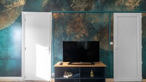 Une pièce avec un téléviseur posé sur un meuble en bois, une porte et un mur orné d’un motif de feuilles.