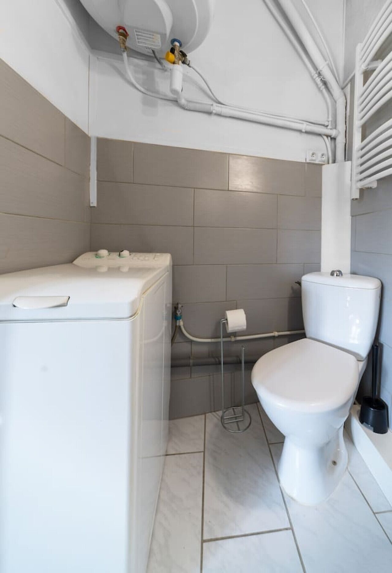 Une petite salle de bain comprenant des toilettes, un lave-linge blanc et un porte-serviettes.