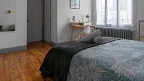 Une chambre avec un plancher en bois, un lit recouvert d’une couvre-lit à motifs floraux, un bureau avec une chaise et un radiateur près de la fenêtre.