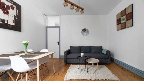 Un salon moderne comprenant un coin repas, un canapé gris, un miroir rond et un luminaire en bois fixé au plafond.
