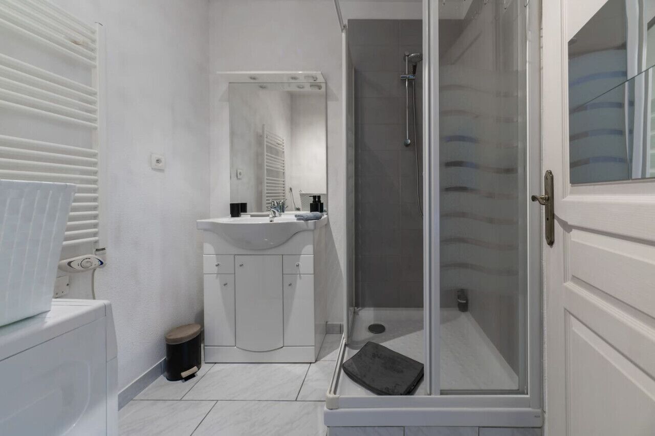 Een moderne badkamer met een douche met glazen wand, een wit wastafel en een spiegel erboven.
