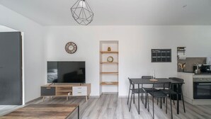 Ein modernes Wohnzimmer mit einem Flachbildfernseher, Holzböden, einem Essbereich mit Stühlen und einer Küche mit Herd.
