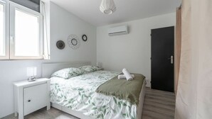 Ein Schlafzimmer mit Bett, Nachttisch, Fenster, Wanddekoration und Klimaanlage.