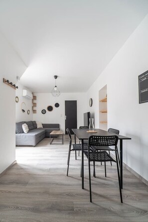 A modern living space with a dining area, a grey sofa, and a black dining table with chairs. - Comfortable Air-cond apartment - city center (Vichy)