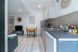 A compact kitchen with a dining area, a TV, and a clock on the wall.