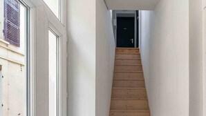A narrow hallway with a wooden staircase leading to a door. - Air-cond duplex apartment in the city center (Vichy)