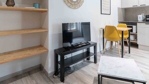 A modern living room with a TV, wooden shelves, a round mirror, and a dining area with yellow chairs. - Air-cond duplex apartment in the city center (Vichy)