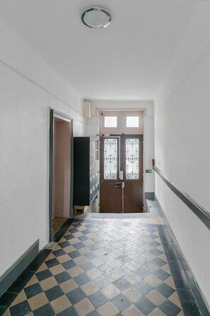 A hallway with patterned floor tiles, a wooden door with decorative glass panels, and a white wall with a small window.