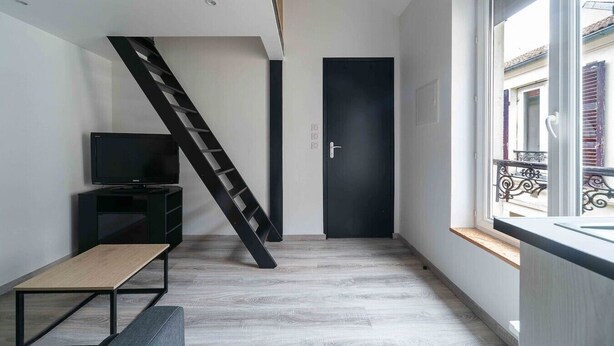 A modern interior with a wooden floor, a black TV stand, a bench, a black door, and a window with a balcony view. - Air-cond duplex apartment in the city center (Vichy)