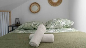 A bedroom with a bed, pillows, a rolled towel, a wall-mounted mirror, and a small table with a lamp. - Air-cond duplex apartment in the city center (Vichy)
