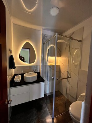 Ein modernes Badezimmer mit rundem Spiegel, Waschbecken und einer Duschkabine aus Glas.