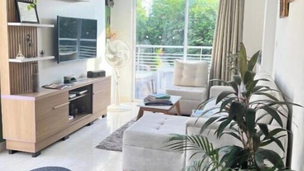 Ein modernes Wohnzimmer mit einer Couch, einem Fernseher, einem Holzschrank und einem großen Fenster mit Blick auf Grünflächen.