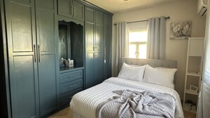 Une chambre à coucher avec un lit, un ventilateur de plafond, une armoire et une fenêtre avec des rideaux.