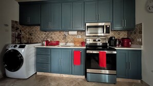 Une cuisine avec des meubles de couleur turquoise, un four à micro-ondes en acier inoxydable, un four noir et un lave-linge.
