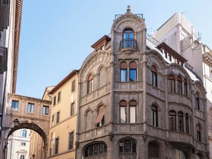 En historisk bygning med detaljeret arkitektur, herunder en balkon med jerngitter og en udsmykket gavl.