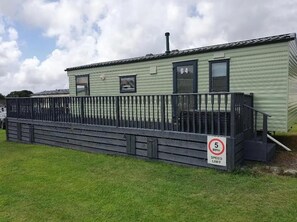 A single-story mobile home with a fenced porch and a speed limit sign of 5 MPH. - Lochside Retreat at Three Lochs Holiday Park (Newton Stewart)