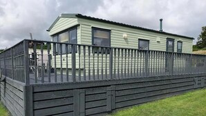 A single-story mobile home with a fenced deck, a chimney, and a number '64' on the side. - Lochside Retreat at Three Lochs Holiday Park (Newton Stewart)
