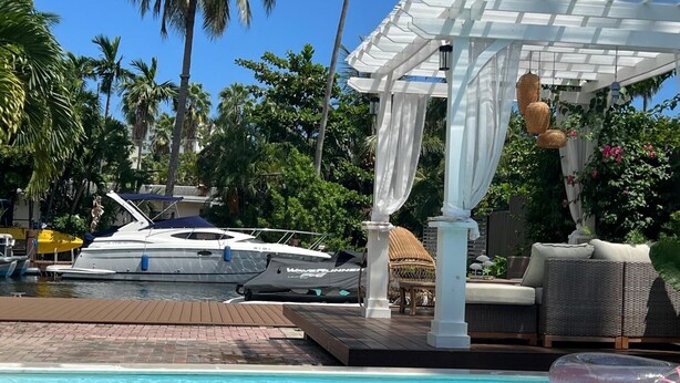 Ein Poolbereich mit weißem Baldachin, Liegestühlen und einem in der Nähe liegenden Yachthafen.