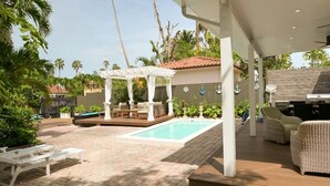 Ein überdachter Außenbereich mit Pool, Liegestühlen und einer Pergola.