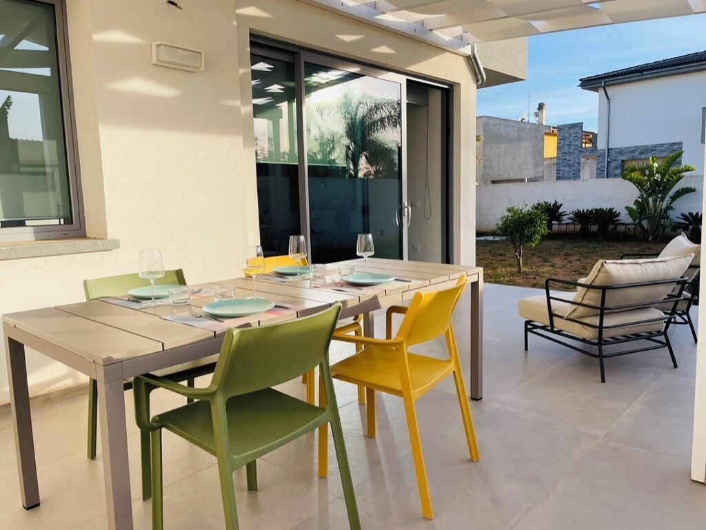 An outdoor dining area with a table and chairs, a sliding glass door, and a view of the surrounding landscape.