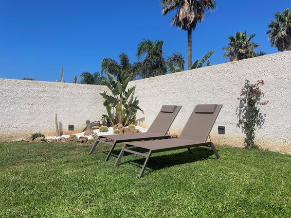Two lounge chairs with a textured wall and palm trees in the background. - Modern Villa in Sicily, comfort, relax, garden and parking (Marsala)
