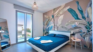 A modern bedroom with a large bed, a sliding glass door to a balcony, and a wall mural of tropical leaves. - Modern Villa in Sicily, comfort, relax, garden and parking (Marsala)
