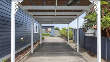 A covered outdoor area with a concrete pathway, white columns, and a blue house in the background.