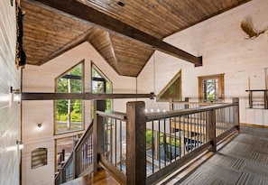 A wooden cabin interior with a loft bedroom, a staircase, and large windows.