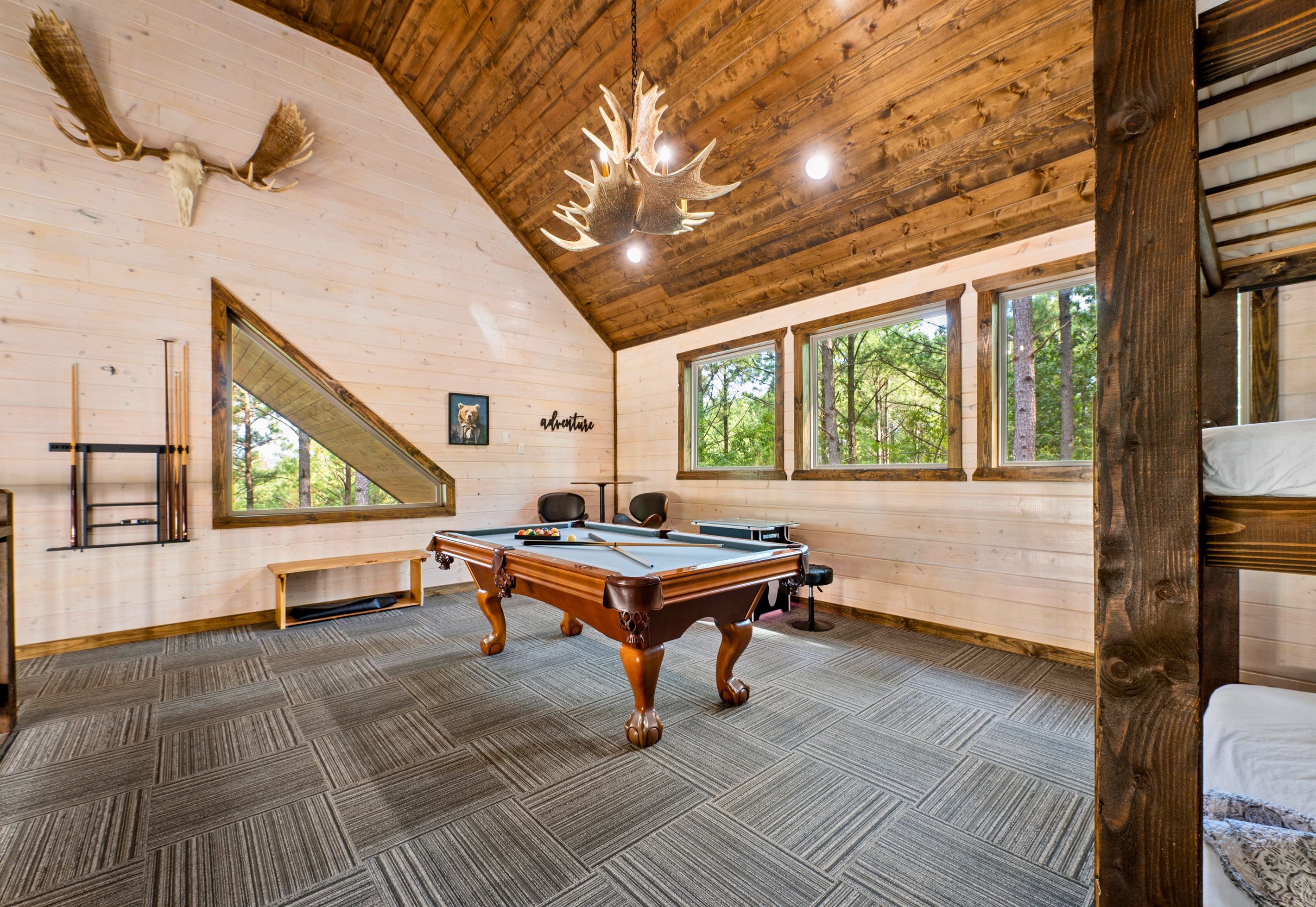 Un interior de madera con mesa de billar, ventanas amplias y un techo con diseño de vigas de madera.