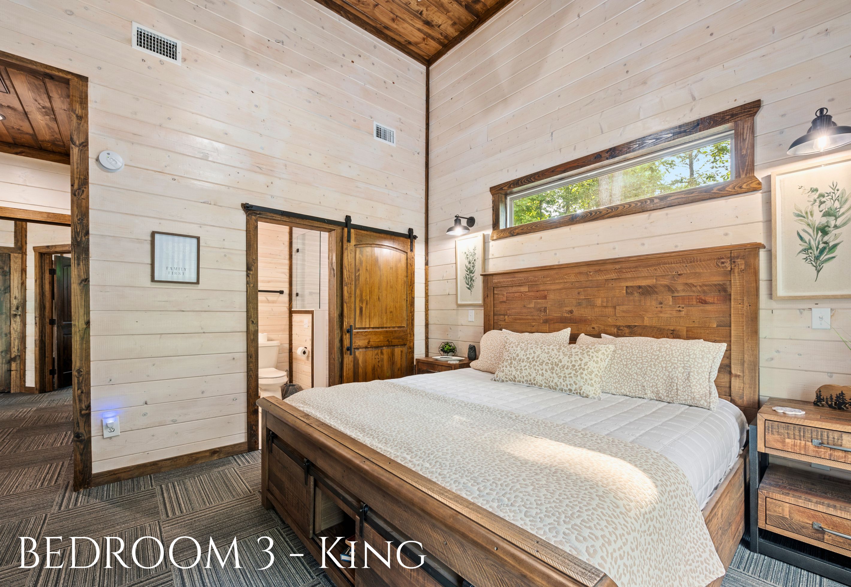 A bedroom with a large bed, wooden headboard, a window with a view, and a door leading to another room.